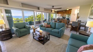A spacious living area with a large sliding glass door leading to a balcony, a teal sofa, a coffee table, and a kitchen in the background. - Sea Forever Vista - Ocean Views From Every Room - 5 Minutes to Magen's Bay Beach (Mandahl)