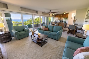 A spacious living area with a large sliding glass door leading to a balcony, a teal sofa, a coffee table, and a kitchen in the background. - Sea Forever Vista - Ocean Views From Every Room - 5 Minutes to Magen's Bay Beach (Mandahl)