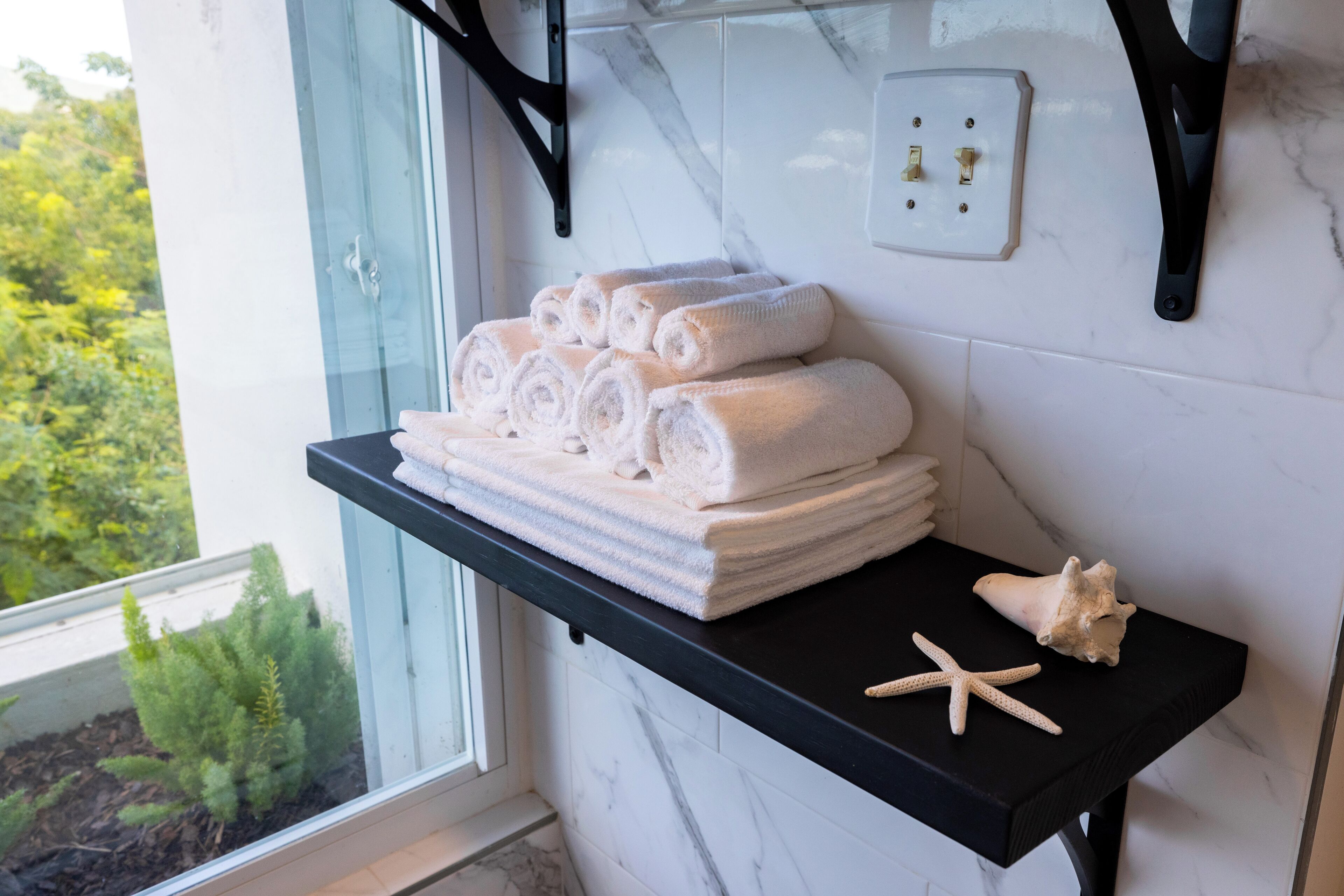 A bathroom with a black countertop holding rolled towels and a starfish decoration.