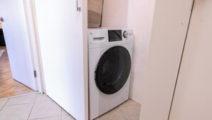 A compact, white front-loading washing machine in a small room with tiled flooring. - Sea Forever Vista - Ocean Views From Every Room - 5 Minutes to Magen's Bay Beach (Mandahl)