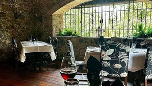 A restaurant with stone walls, tables set with white tablecloths, and a view through a window with metal bars. - Sea Forever Vista - Ocean Views From Every Room - 5 Minutes to Magen's Bay Beach (Mandahl)