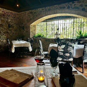 A restaurant with stone walls, tables set with white tablecloths, and a view through a window with metal bars. - Sea Forever Vista - Ocean Views From Every Room - 5 Minutes to Magen's Bay Beach (Mandahl)