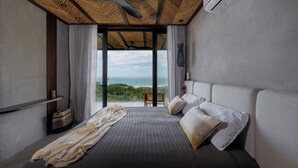 Ein modernes Schlafzimmer mit einem großen Bett, einem Deckenventilator und Blick auf den Ozean.