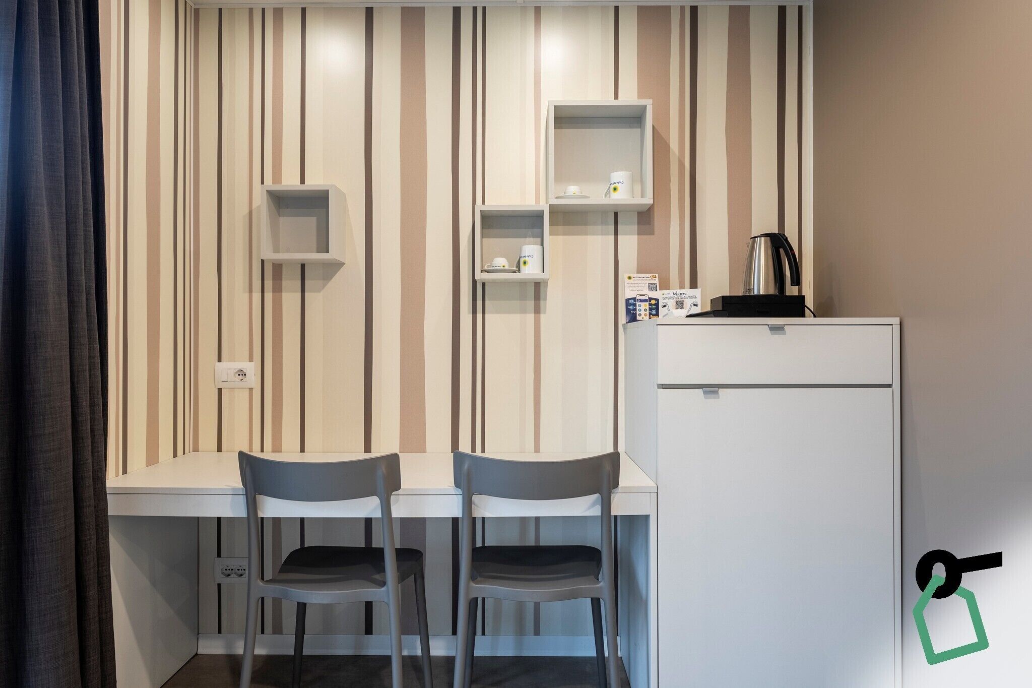 A small kitchenette with a white refrigerator, two chairs, and a striped wall.