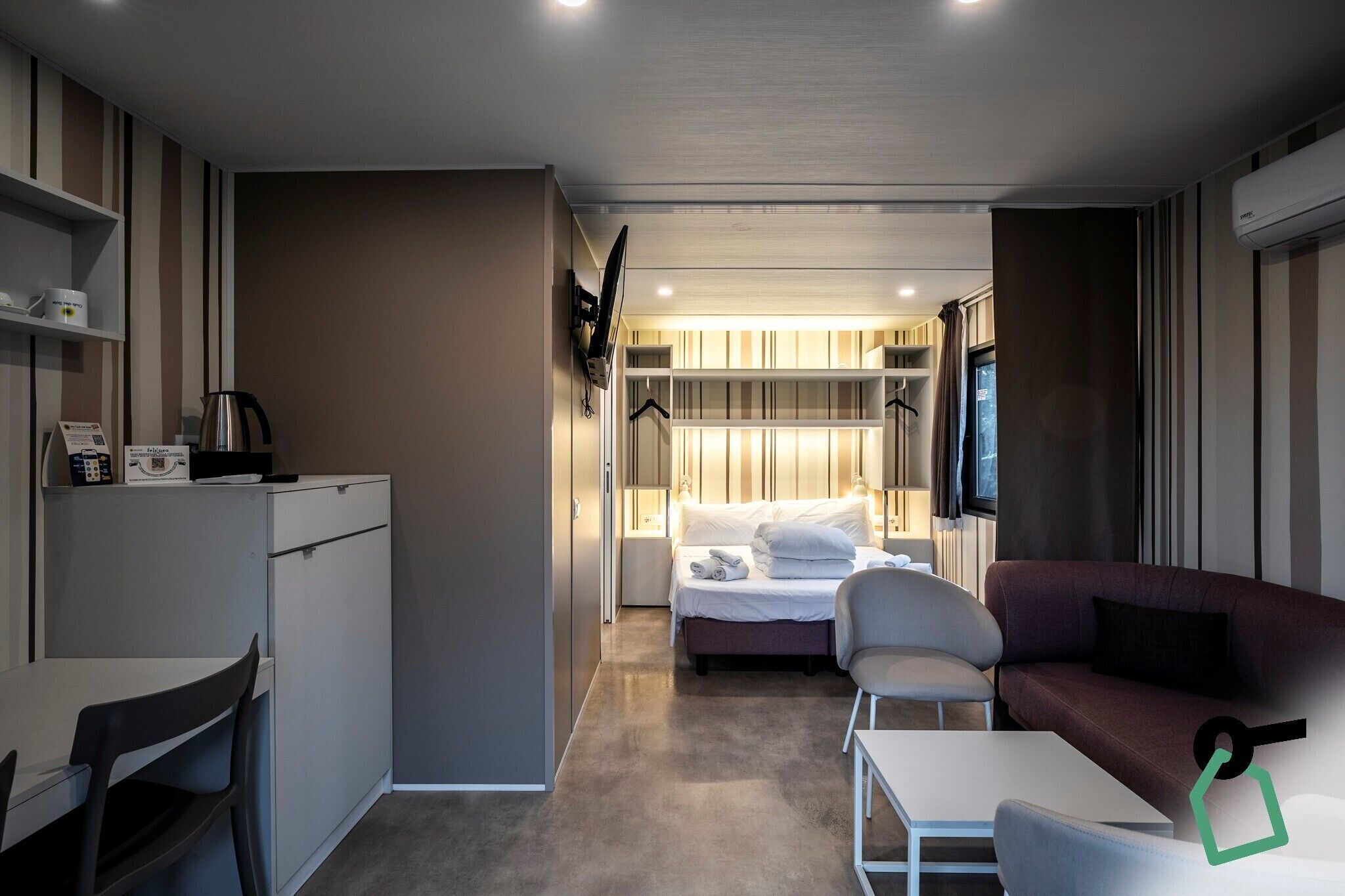 Een kleine hotelkamer met een bed, een slaapbank, een bureau en een stoel.