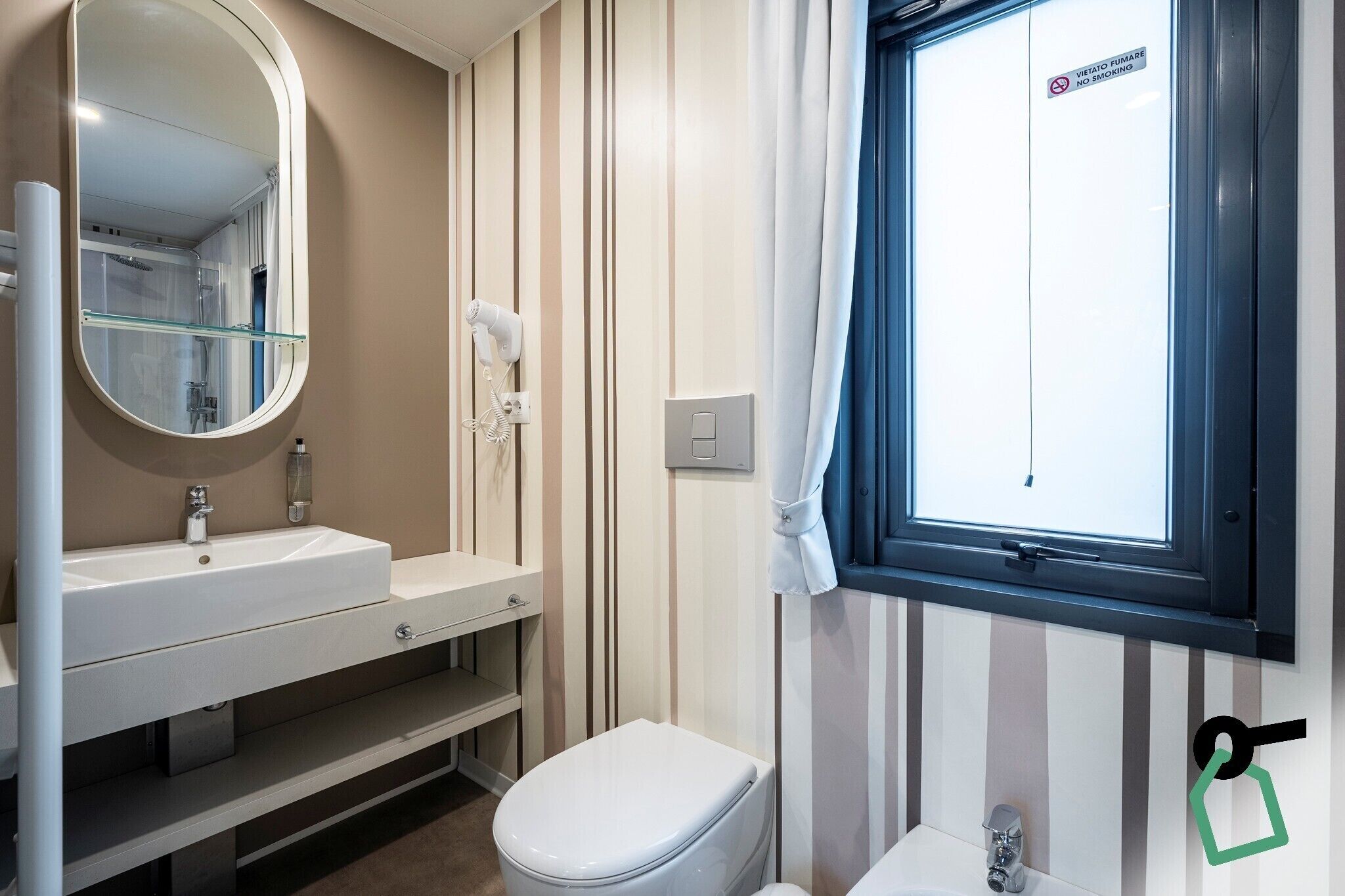 Een badkamer met een wit wastafel, spiegel en toilet. Er is een raam met uitzicht op buiten.