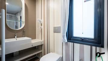 Een badkamer met een wit wastafel, spiegel en toilet. Er is een raam met uitzicht op buiten.