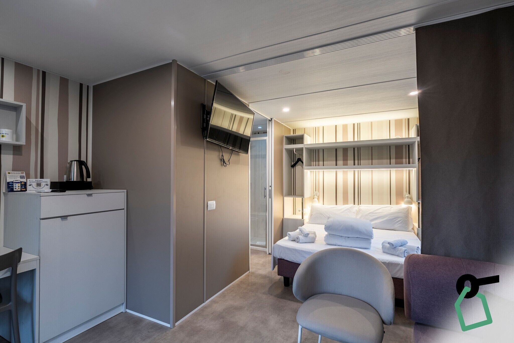 Una camera d'albergo compatta con un letto, un comodino e un angolo cottura.