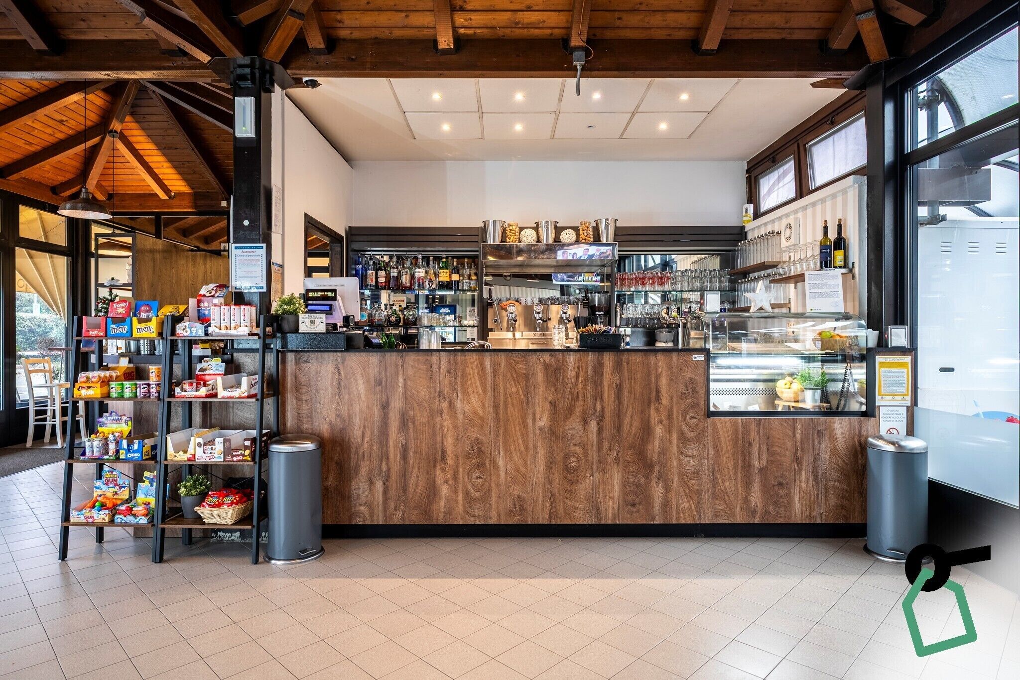 Een moderne bar met een houten toonbank, planken vol snacks en diverse flessen.