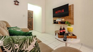 Ein Wohnzimmer mit einer Couch, einem Couchtisch mit Fernbedienung, einer Popcornschüssel und einem an der Wand montierten Netflix-Fernseher.