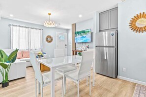 A modern living room with a white sofa, a glass dining table, and a kitchen area with a stainless steel refrigerator. - Honolulu Central 1 Bd 1 Ba (Honolulu)