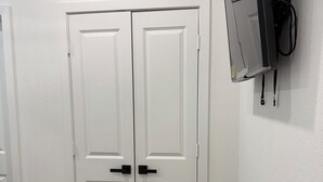 Een kamer met twee witte deuren, een wandgemonteerde flatscreen-televisie en een houten vloer.