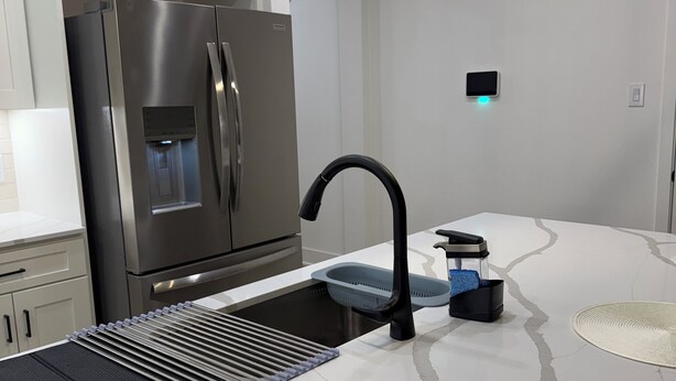 Een moderne keuken met een roestvrijstalen koelkast, een ingebouwde waterdispenser, een zwarte kraan en een strak aanrecht.