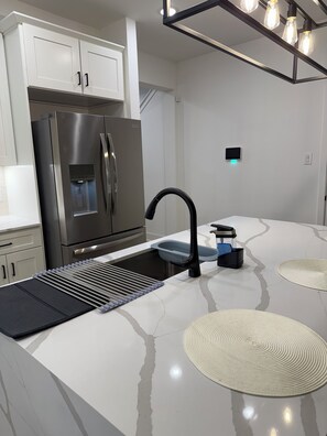 A modern kitchen with a stainless steel refrigerator, a built-in water dispenser, a black faucet, and a sleek countertop. - Luxury home II Near NRG, Med Center, Downtown (Houston)