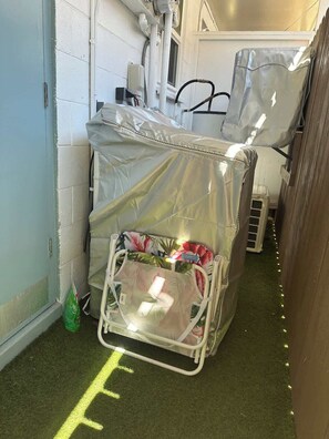 A small, enclosed space with a bed covered in a protective sheet, a green bag on the floor, and a yellow line marking on the floor. - One Bed Honolulu Kaaha (Honolulu)