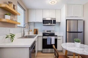 A modern kitchen with white cabinets, stainless steel appliances, and a marble island. - One Bed Honolulu Kaaha (Honolulu)