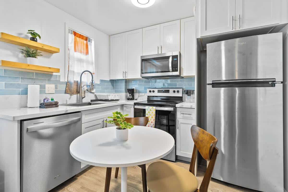 A modern kitchen with white cabinets, stainless steel appliances, a round dining table, and a potted plant.