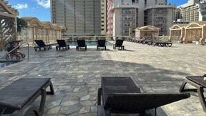 A rooftop pool area with lounge chairs and a swimming pool, surrounded by high-rise buildings. - Island Colony Waikiki High-Rise 1BR with Split AC & Full Kitchen (Honolulu)