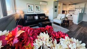 A modern living room with a black sofa, a white armchair, and a kitchen area with white cabinets. - Island Colony Waikiki High-Rise 1BR with Split AC & Full Kitchen (Honolulu)