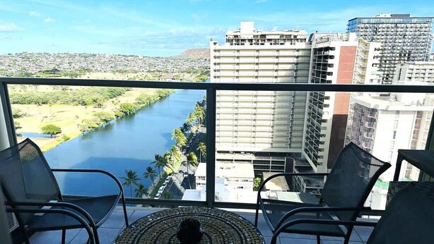 A balcony with two chairs and a table, overlooking a river and cityscape. - Island Colony Waikiki High-Rise 1BR with Split AC & Full Kitchen (Honolulu)