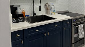 Une cuisine avec des meubles hauts blancs, un évier noir et une cuisinière.