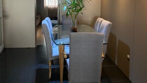 Un comedor moderno con una mesa de vidrio, cuatro sillas grises tapizadas y una planta en maceta.