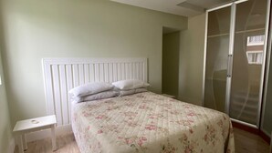 Un dormitorio con cama, mesita de noche, armario y lámpara en el techo.