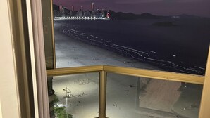 Habitación de esquina con vista a la playa y al horizonte urbano de noche.