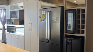 Una cocina moderna con un refrigerador de acero inoxidable, un mini refrigerador negro y un horno empotrado. Hay un taburete de bar frente a la encimera.