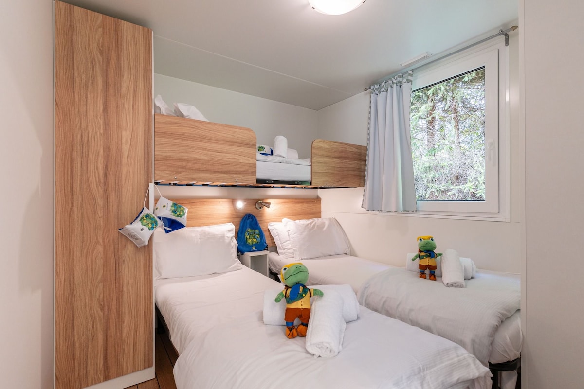 A hotel room with two beds, a wardrobe, a window with curtains, and a stuffed toy on one bed.