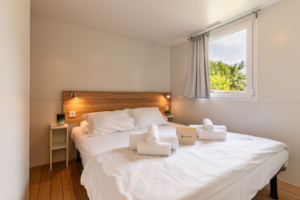A hotel room with a bed, bedside lamps, a window with curtains, and a view of greenery outside.