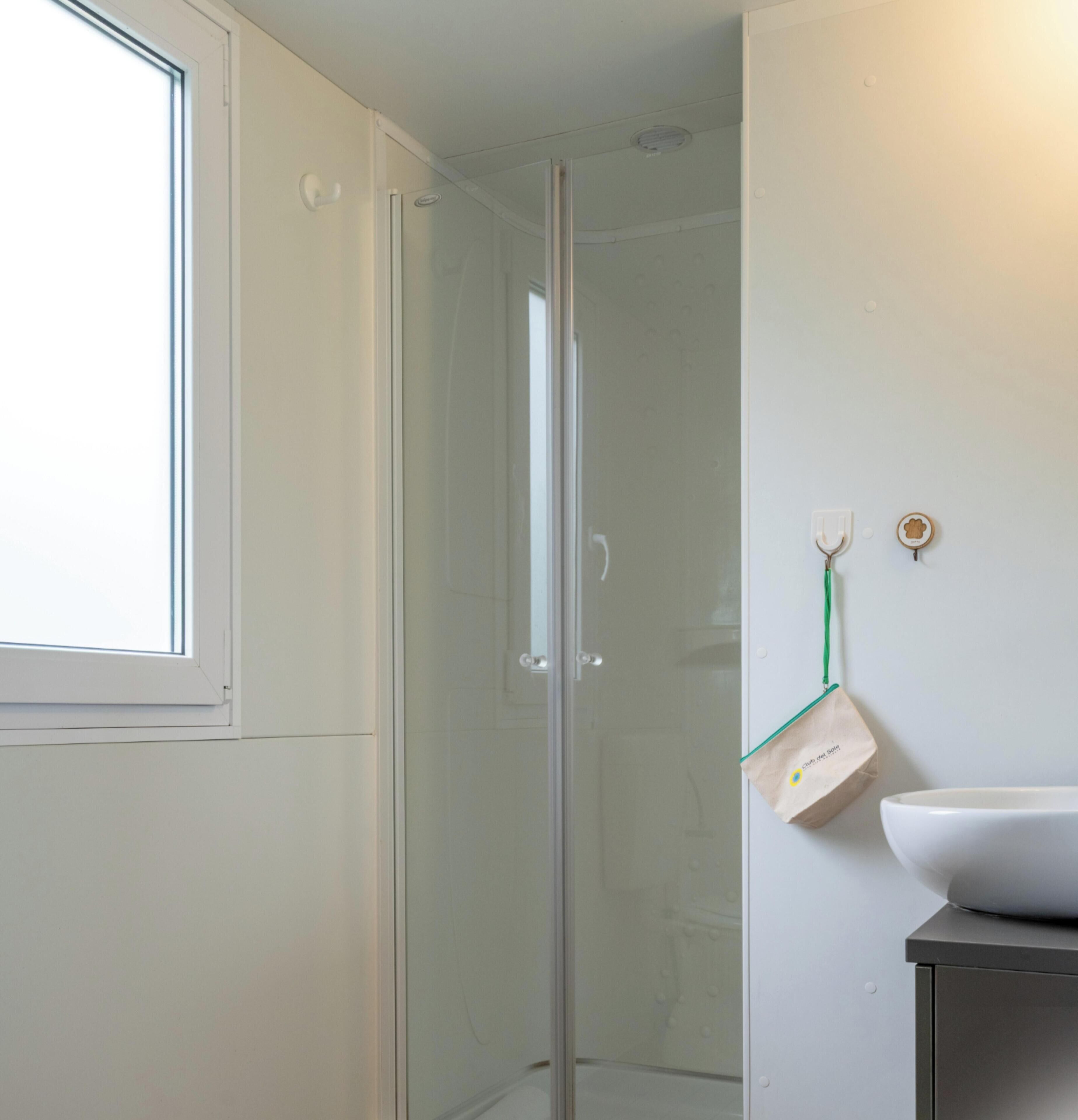 A bathroom with a glass shower enclosure, a white sink, and a window.