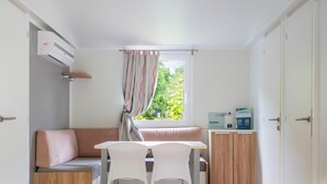 A room with a sofa, a table with two chairs, a window with curtains, a cabinet with items, and an air conditioning unit. - Hotiday Lago di Levico (Levico Terme)