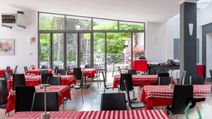 A restaurant with red and white checkered tablecloths, black chairs, and large windows offering a view of greenery outside. - Hotiday Lago di Levico (Levico Terme)
