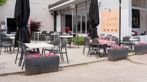 An outdoor cafe area with tables and chairs, a large sign with the cafe's name, and a building entrance. - Hotiday Lago di Levico (Levico Terme)