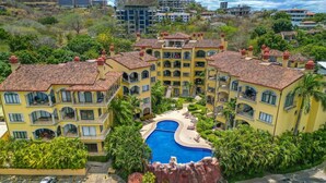 Um hotel com vários andares, piscina central rodeada por vegetação exuberante e palmeiras.