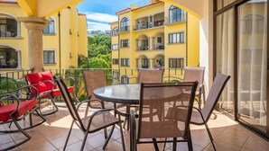 Varanda com mesa redonda e cadeiras, com vista para um edifício amarelo com varandas.