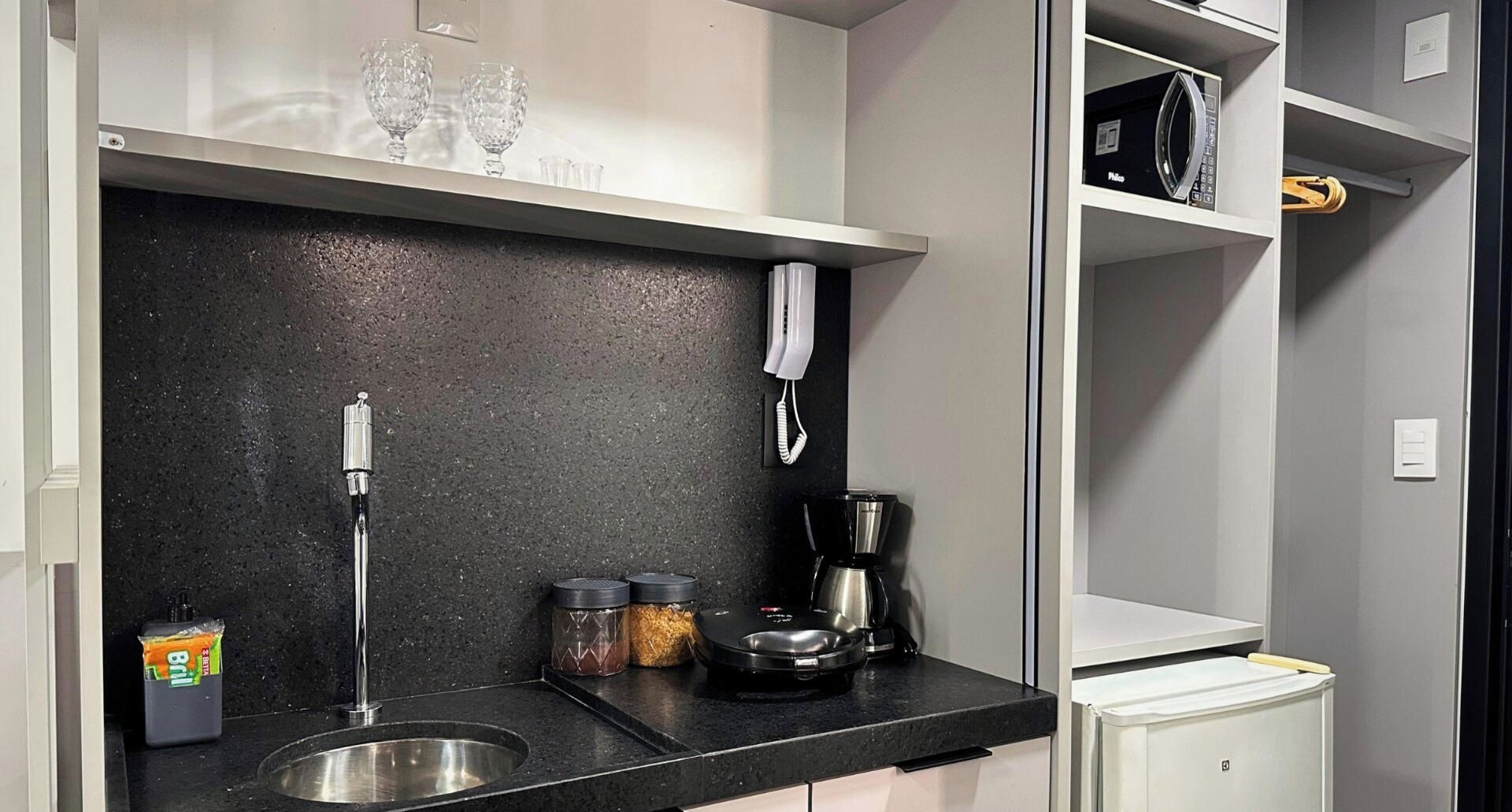 Cocina compacta con pileta, cafetera y frascos de almacenamiento.