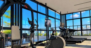 Ein Fitnessstudio mit Trainingsgeräten, großen Fenstern und Blick auf die Stadt.