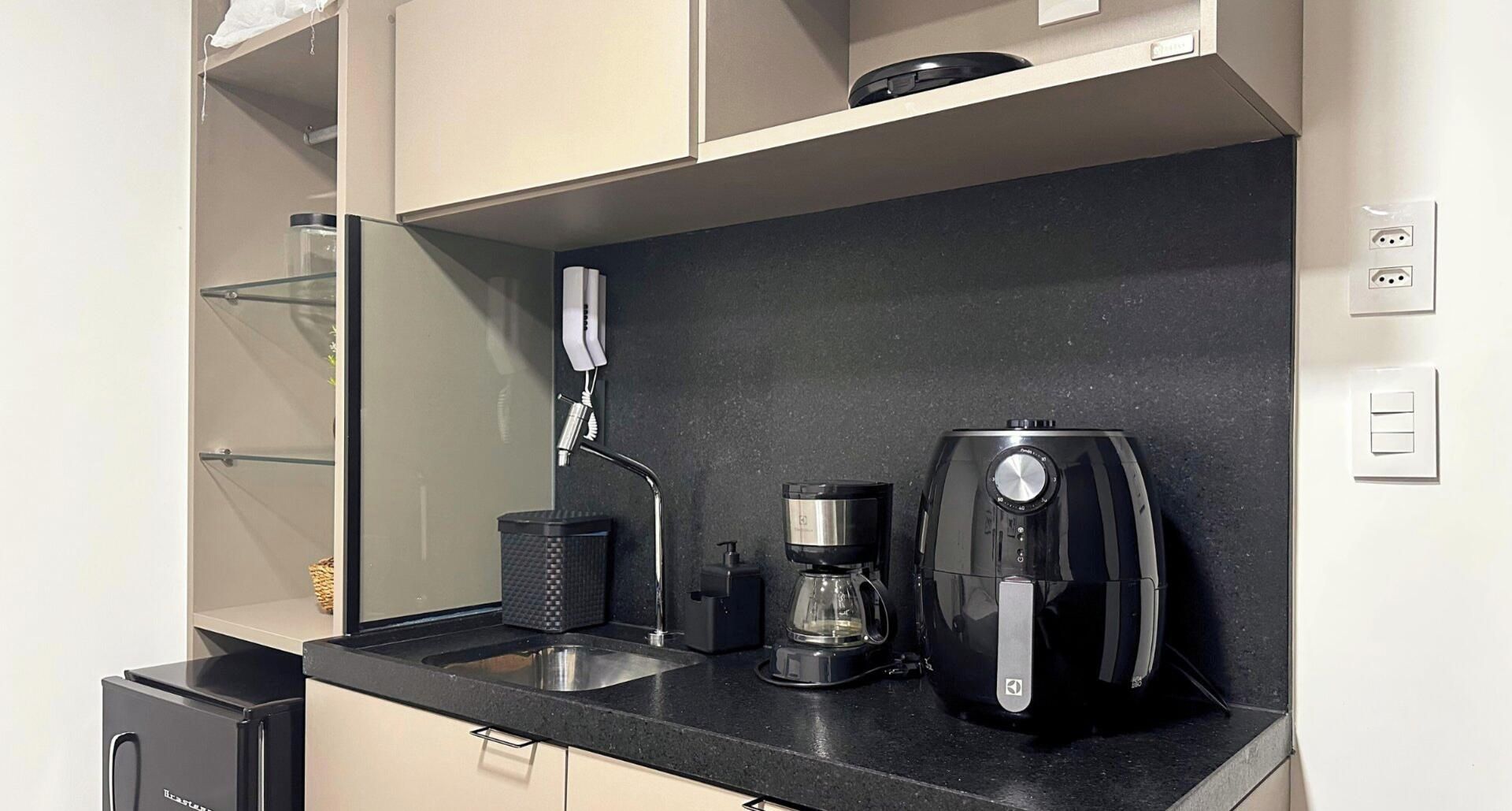 A kitchenette with a coffee maker, a kettle, and a small trash bin.