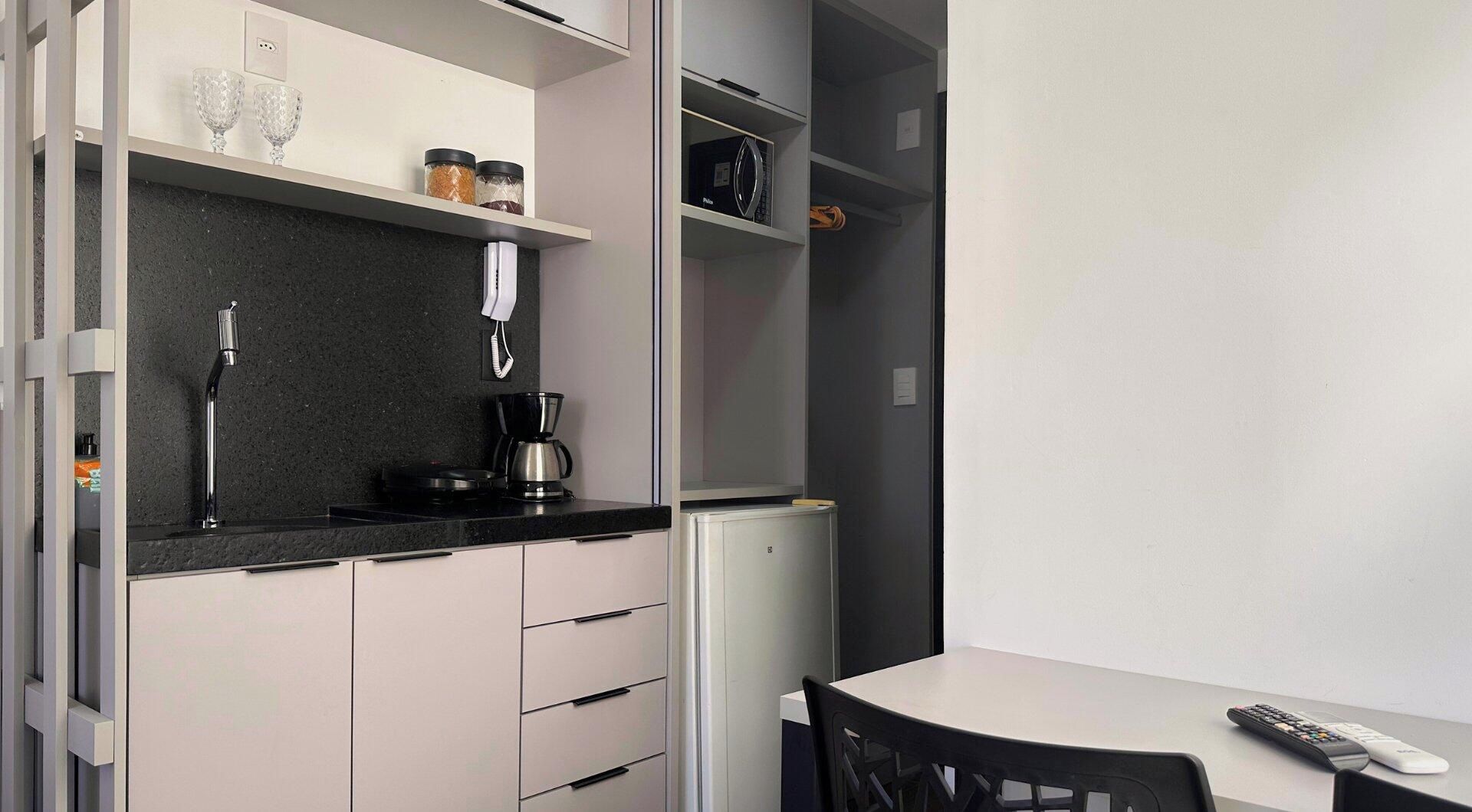 A compact kitchen with a coffee maker, a kettle, and a microwave on the countertop.