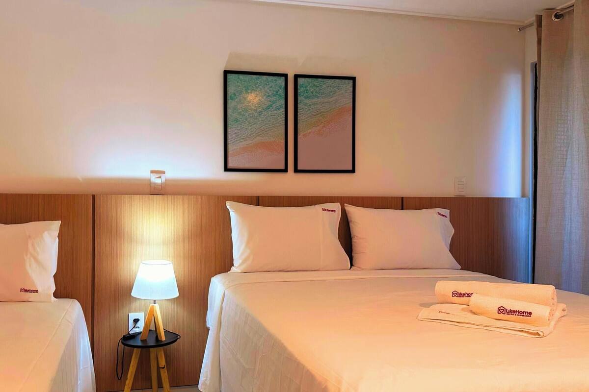 Habitación de hotel con dos camas, una mesita de noche con lámpara y dos cuadros en la pared.
