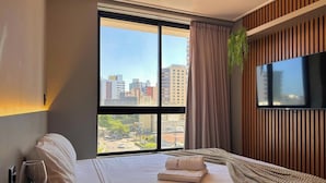 Een hotelkamer met een groot raam, een bed, een flatscreen-televisie en een potplant.