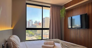 Ein Hotelzimmer mit großem Fenster, einem Bett, einem Flachbildfernseher und einer Zimmerpflanze.