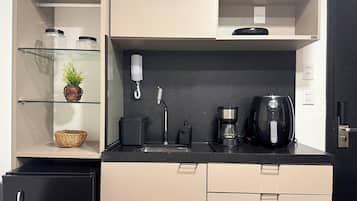 Eine kleine Küche mit Kaffeemaschine, Wasserkocher und Spüle. Es gibt Schränke mit Griffen und einen kleinen Korb auf der Arbeitsfläche.