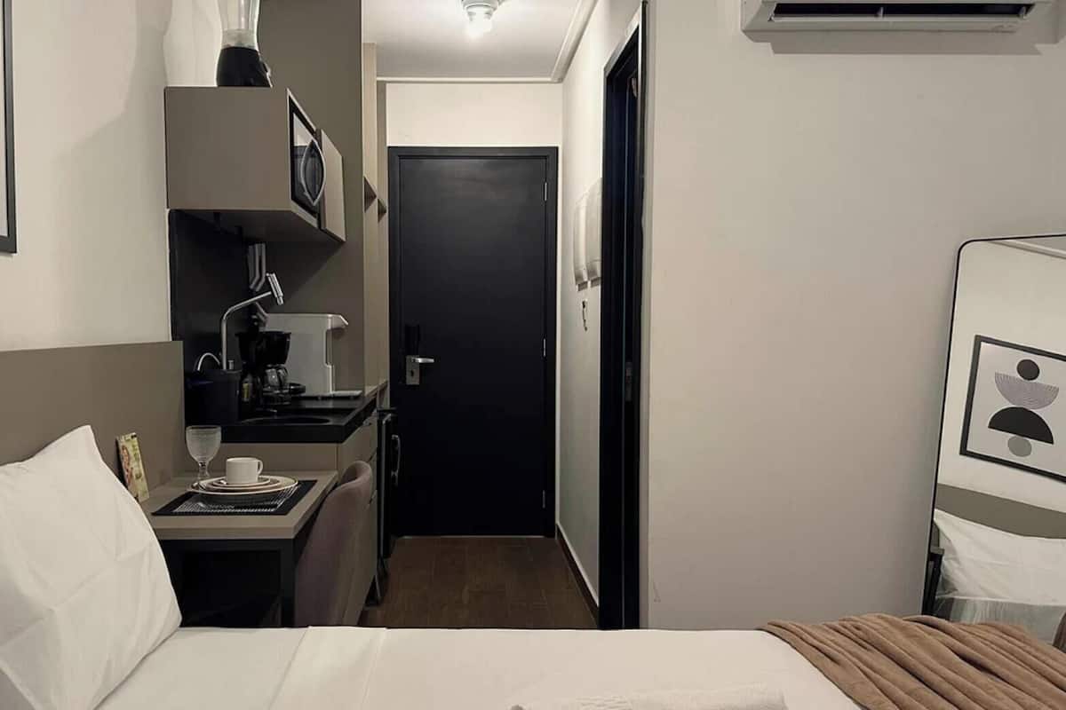 Habitación de hotel con cama, escritorio con cafetera, un cuadro en la pared y un equipo de aire acondicionado.
