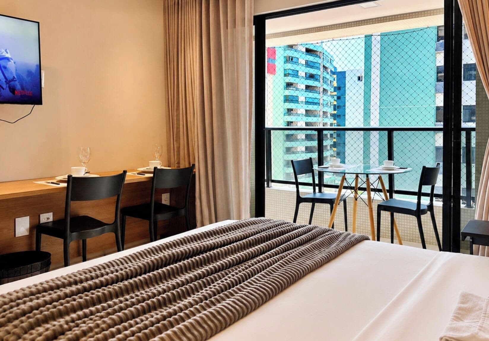 Una habitación de hotel con cama, escritorio y balcón con sillas.