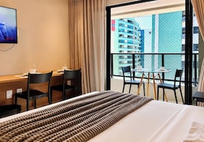 Quarto de hotel com cama, escrivaninha e varanda com cadeiras.