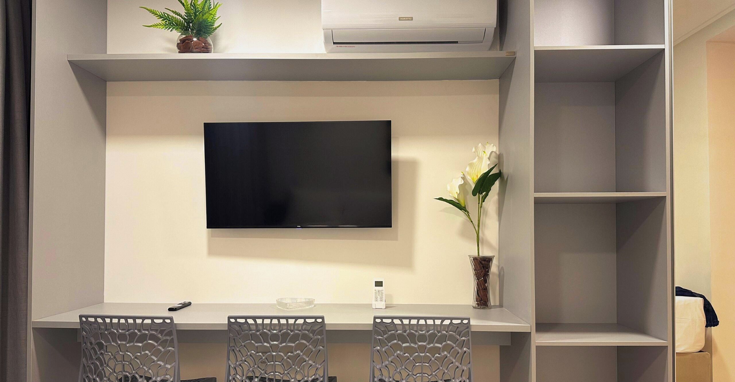 Una habitación moderna con televisor de pantalla plana en la pared, una pequeña mesa con sillas y una planta en maceta.