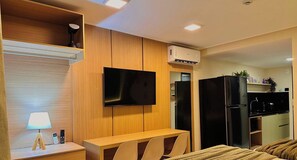 Een moderne slaapkamer met een houten hoofdbord, een flatscreen televisie aan de muur, een nachtkastje met een lamp, en een bed met een bruine deken.